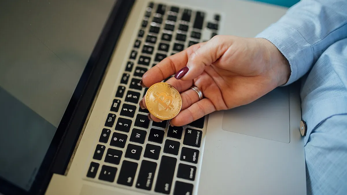 Une pièce de Bitcoin tenue au-dessus d’un ordinateur portable